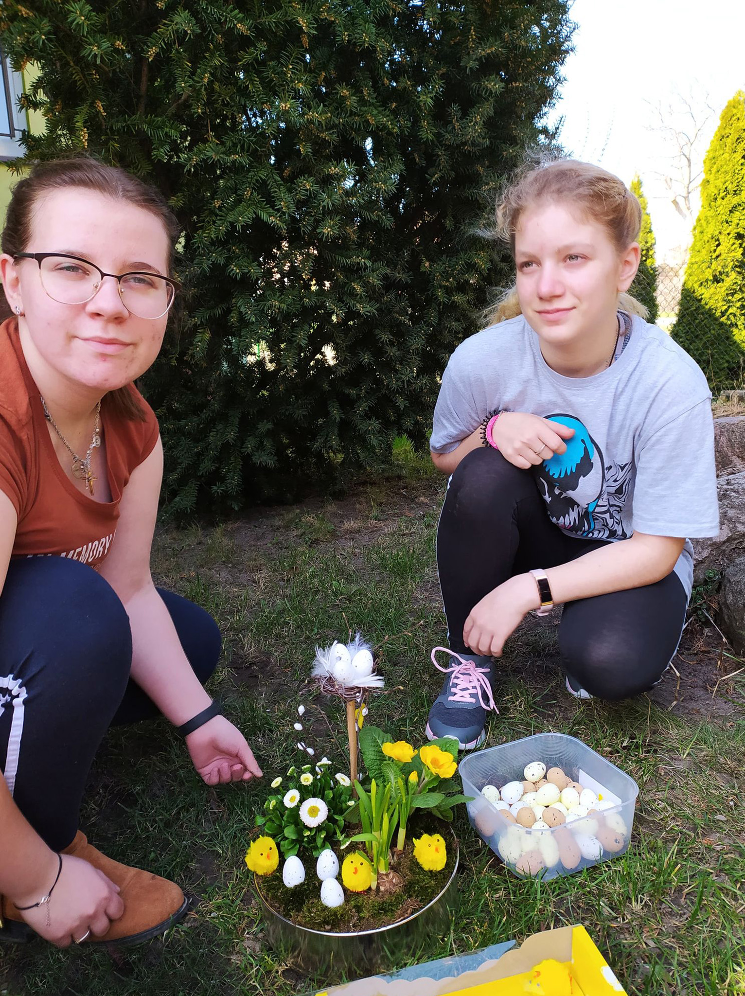 dziewczyny kucają na dworze ze stoikiem z żywych kwiatów w blaszce do pieczenia