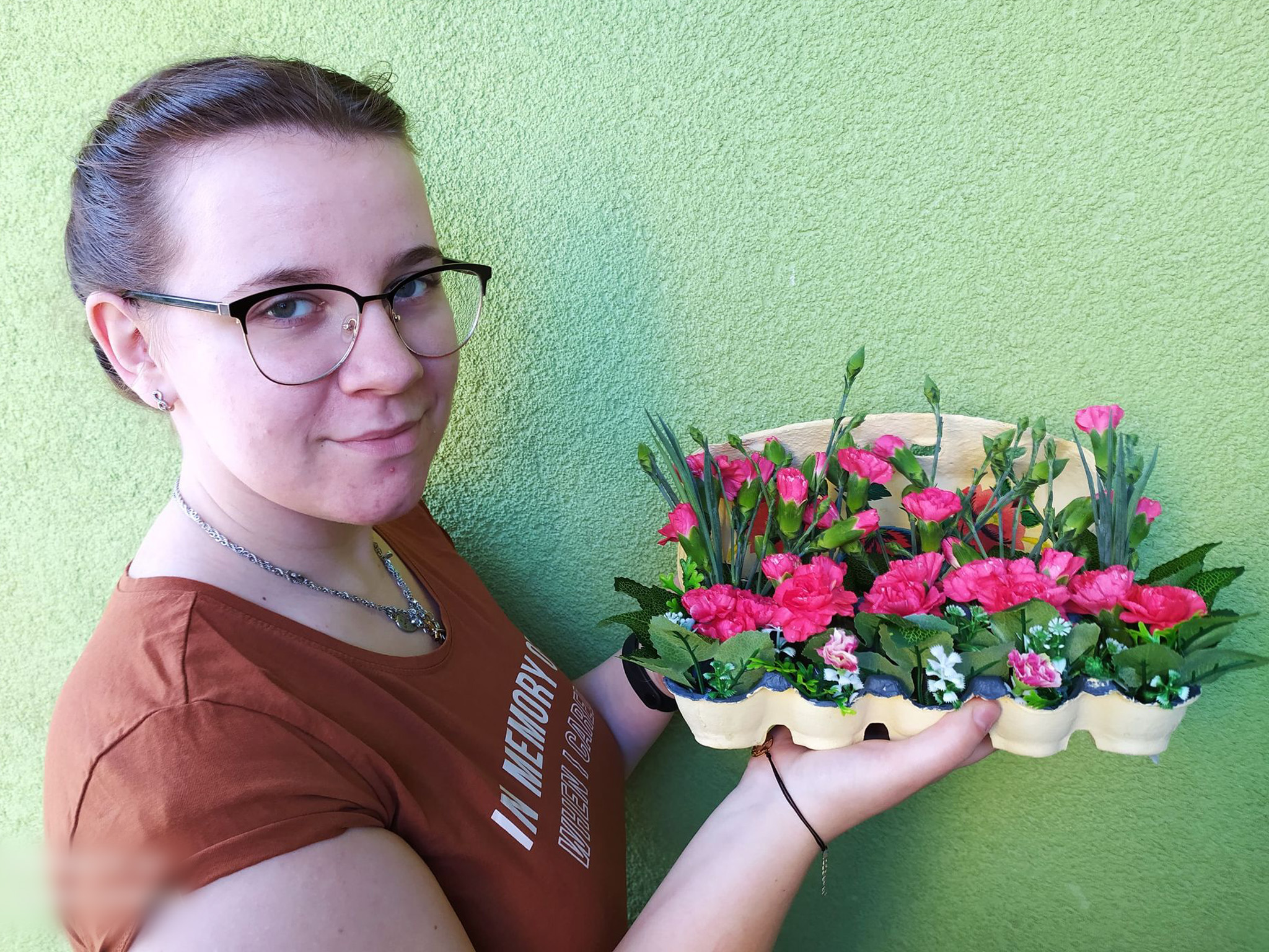 wychowanka prezentuje stroik z żywych kwiatów w wytłaczance po jajach
