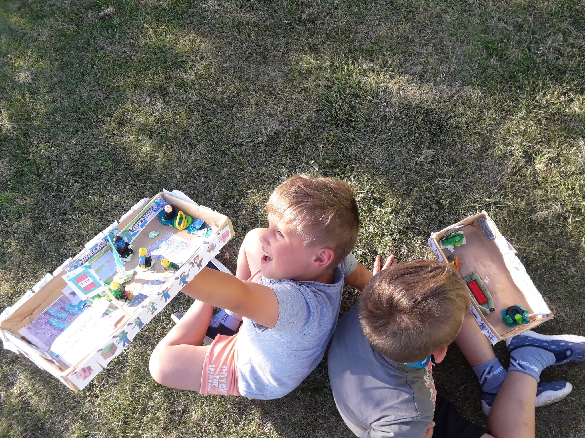 Chłopaki siedzą na trawie z pudełkami