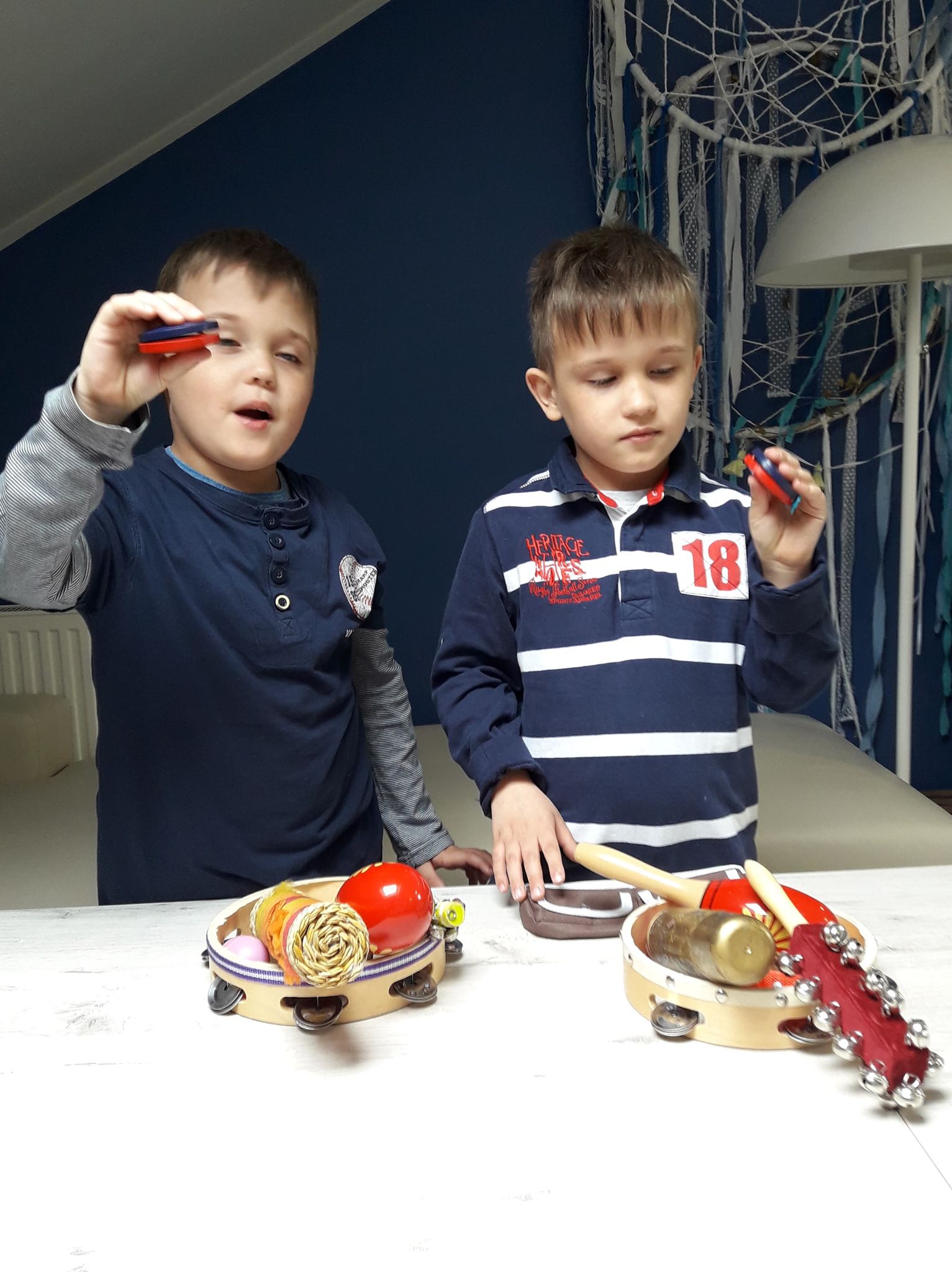 dwaj chłopcy stoją przy stole z instrumentami, grają na kastanietach