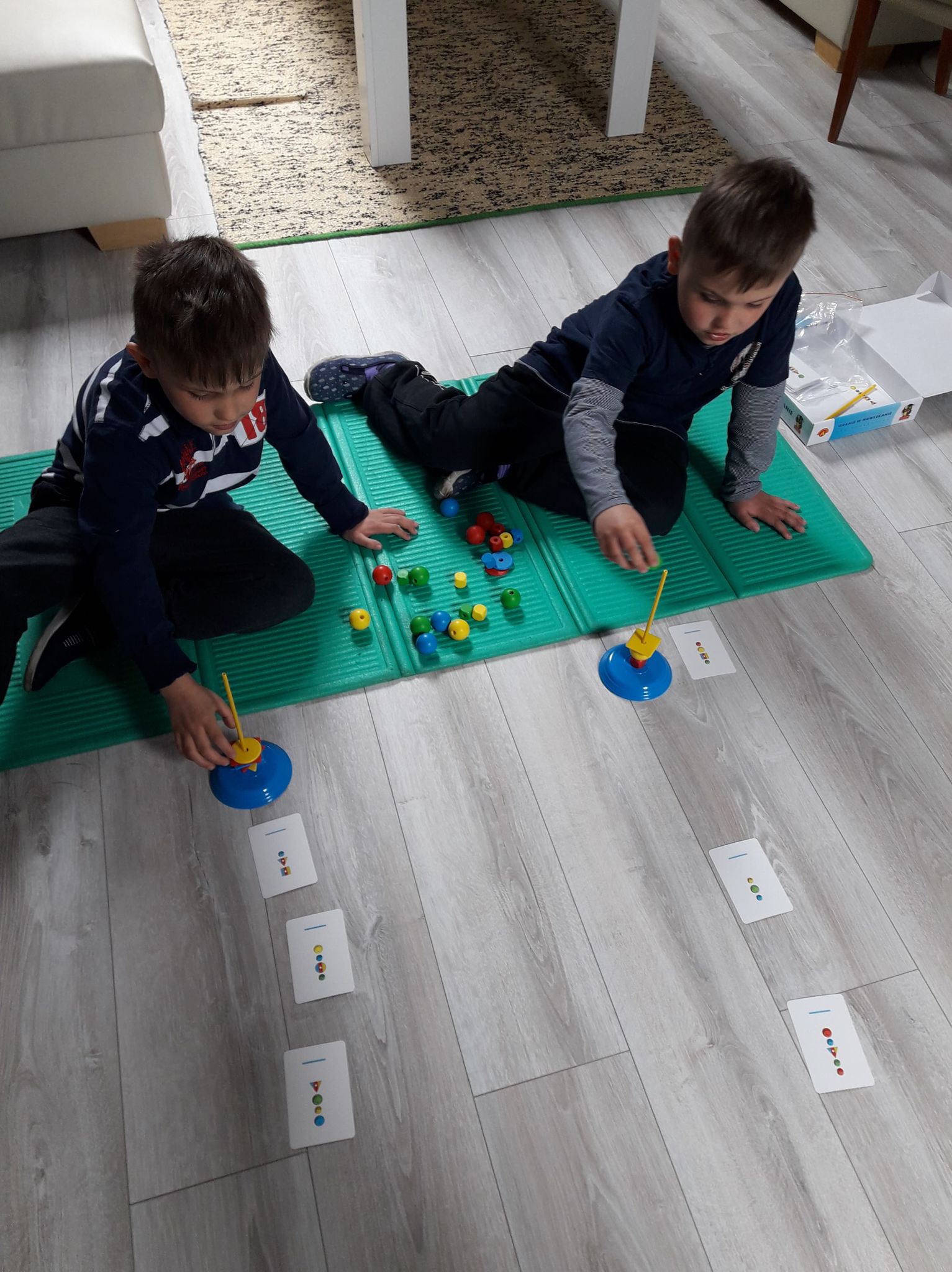 dwaj chłopcy na podłodze nawlekają kolorowe klocki