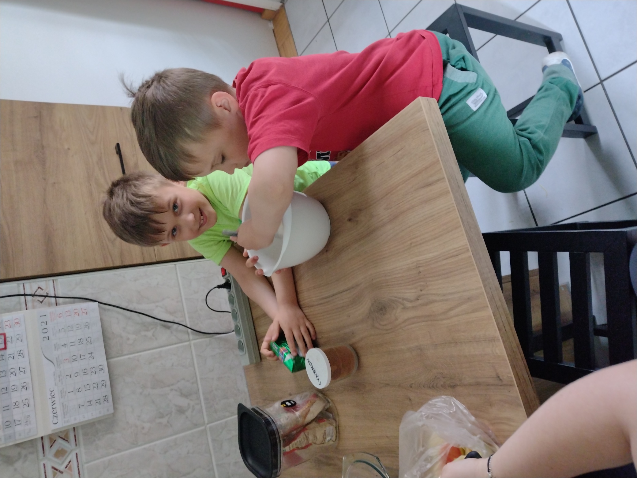 chłopcy siedzą przy stole, Julek miesza składniki ciasta w misce