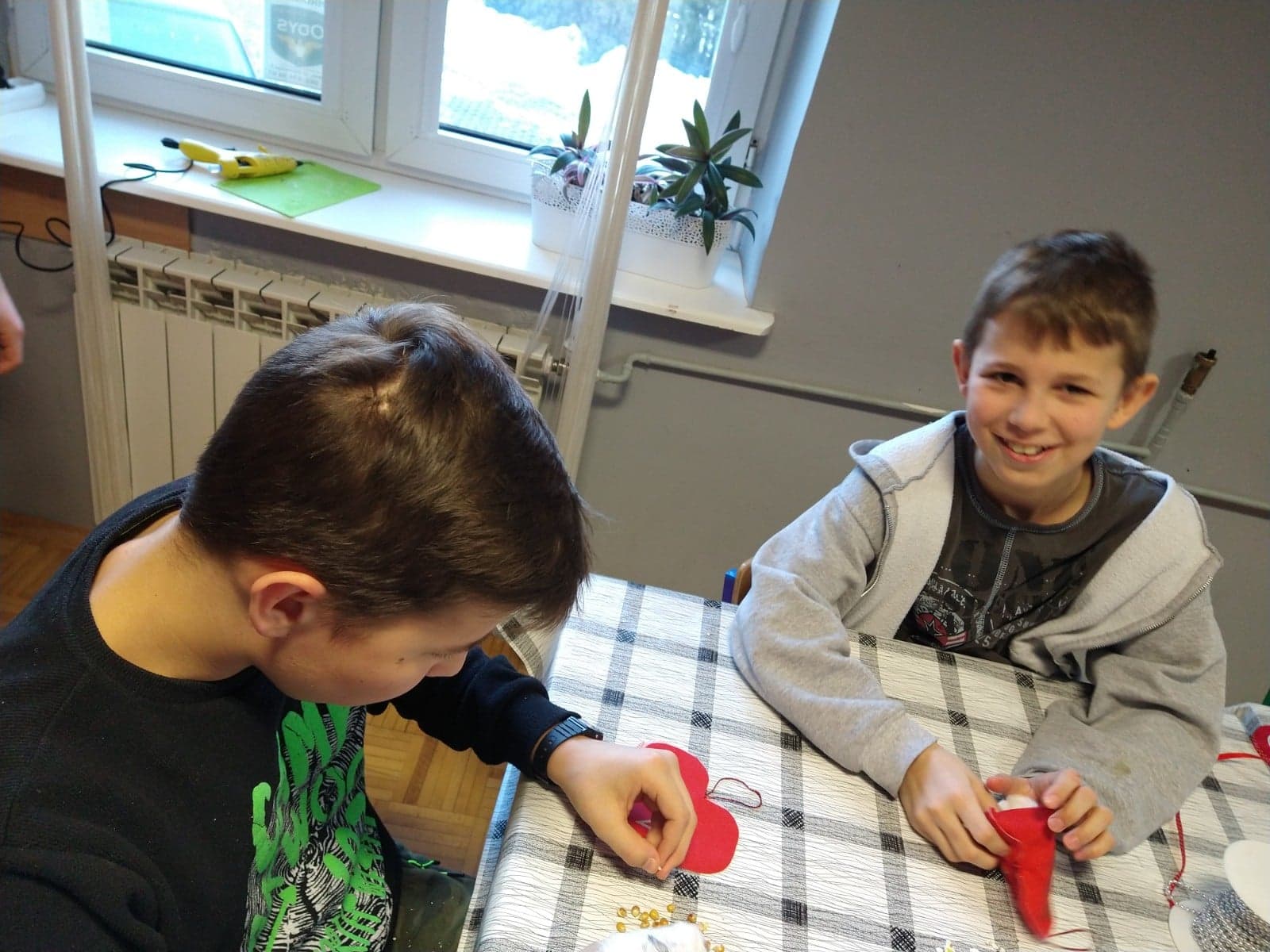chłopcy Paweł i Kacper siedzą przy stole i wypełniają watą materiałowe serca