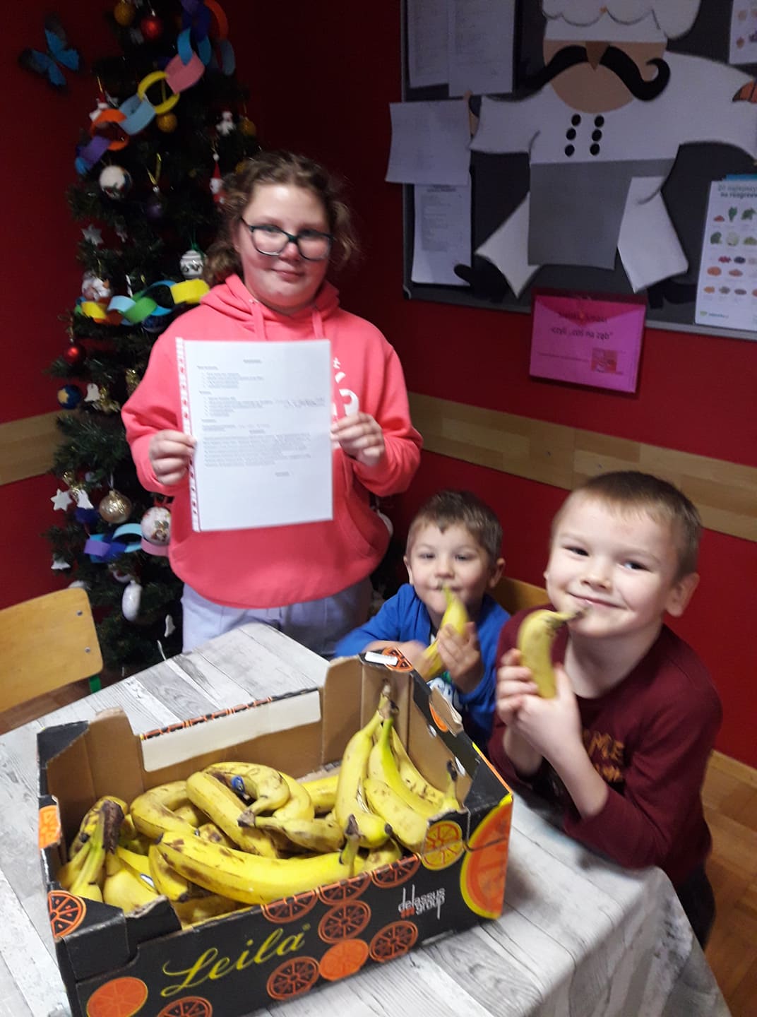 Dzieci siedzą przy stole z bananami, Agatka pokazuje przepis na bananowca