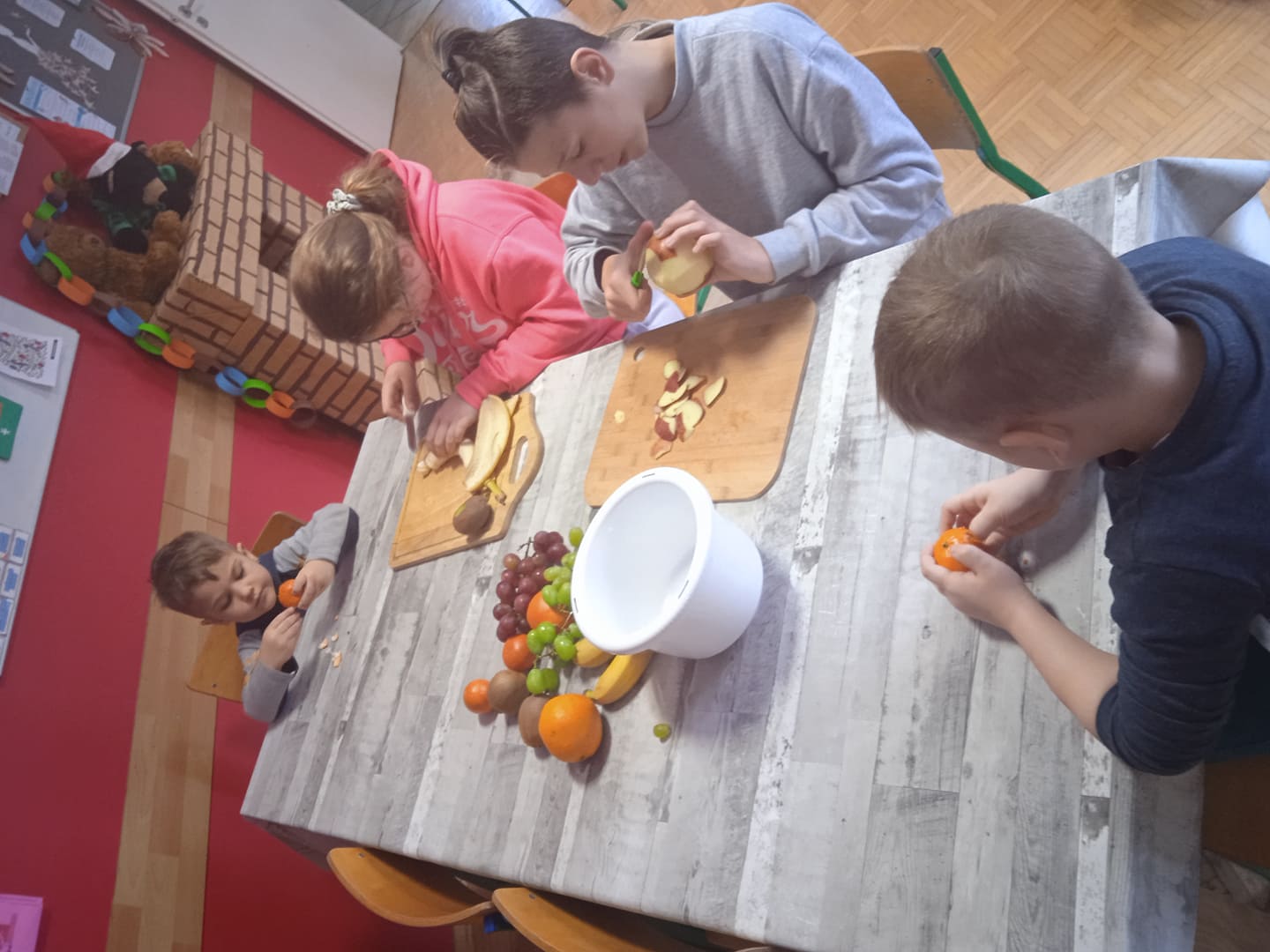 dzieci przy stole robią sałatkę owocową