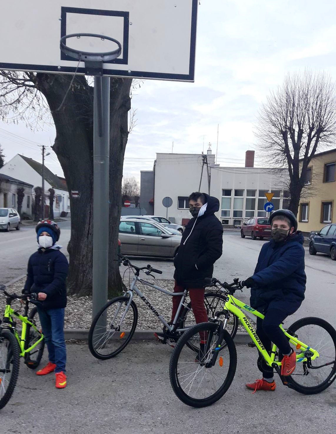 trzej chłopców stoi z rowerami na parkingu (w tle auta na parkingu)